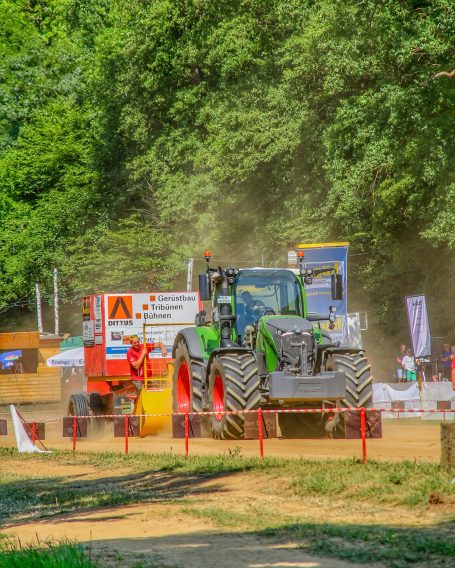 Traktor und Anhänger bewegen sich durch eine staubige Offroad-Strecke.
